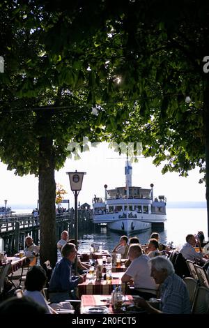 Leute sitzen in einem Biergarten mit Dampfschiff und Pier im Hintergrund, Herrsching, Ammersee, Bayern, Deutschland Stockfoto