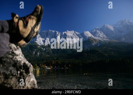 Füße hoch, Mann ruht am Ufer des Eibsees, Zugspitze im Hintergrund, Bayern, Deutschland Stockfoto