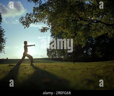 Entspannende Frau bei einem Yoga-Training im Parkbereich eines Wellnesshotels bei Sonnenuntergang in der Nähe von Hameln, Niedersachsen Stockfoto