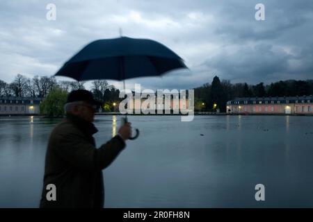 Mann, der am Schloss Benrath mit Schirm vorbeigeht, Düsseldorf, Landeshauptstadt von NRW, Nordrhein-Westfalen, Deutschland Stockfoto