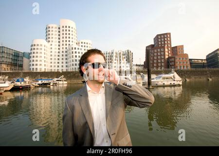 Junger Geschäftsmann, der ein Mobiltelefon benutzt, moderne Architektur von Frank Gehry, Bürogebäude, Media Harbour, Neuer Zollhof, Düsseldorf, Staat c Stockfoto