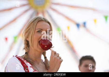 Eine Frau, die Dirndl-Kleid trägt und kandierten Apfel isst Stockfoto