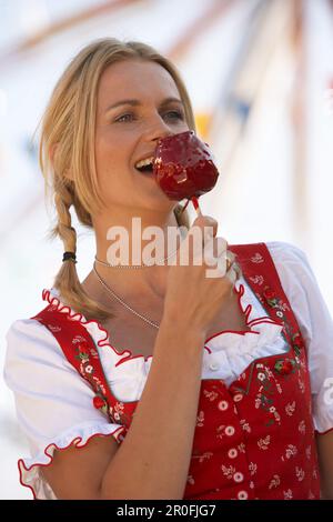 Eine Frau, die Dirndl-Kleid trägt und kandierten Apfel isst Stockfoto