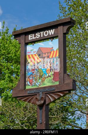 Elstow-Dorfschild, mit alter Marktszene vor der Moot Hall, am Grünen, Elstow Stockfoto