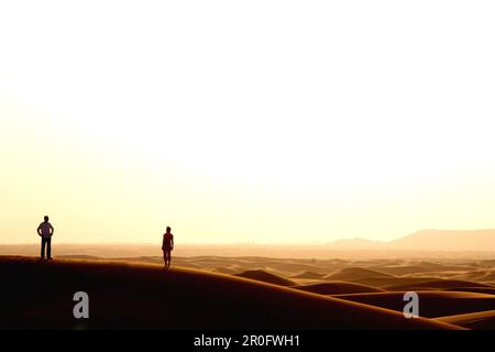 Silhouette eines Paares in der Wüste, das den Sonnenuntergang beobachtet, Dubai, Vereinigte Arabische Emirate, VAE Stockfoto