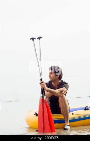 Junger Mann sitzt auf einem Schlauchboot, Ammersee, Bayern, Deutschland Stockfoto