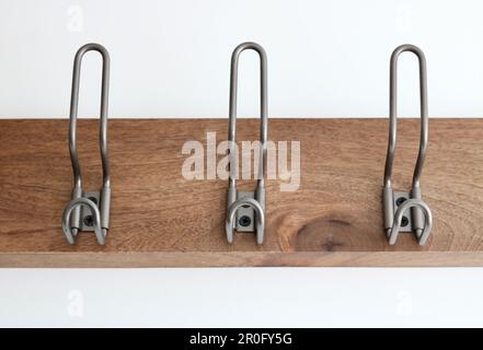 Drei Kleiderhaken aus Metall an einer Holzplatte, die an der weißen Wand befestigt ist Stockfoto