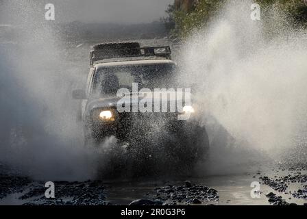 Ein Geländefahrzeug, das durch ein Flussbett, die Al Hajar Berge, Wadi Bani auf, Oman, Asien fährt Stockfoto