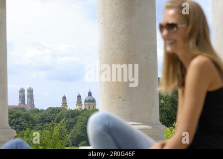 Junge Frau sitzt in Monopteros, Frauenkirche und Theaterkirche, englischer Garten, München, Bayern, Deutschland Stockfoto