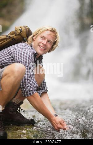 Junger Mann, der vom Wasserfall trinkt, Werdenfelser Land, Bayern, Deutschland Stockfoto