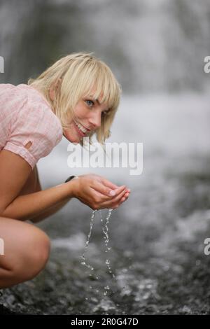 Junge Frau, die Wasser aus dem Wasserfall trinkt, Werdenfelser Land, Bayern, Deutschland Stockfoto