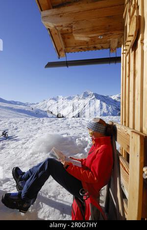 Weibliche Skifahrerin im Hinterland, die sich vor einer alpinen Lodge ausruht, während sie eine Karte liest, Hirzer, Tux Alps, Tirol, Österreich Stockfoto