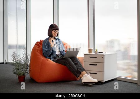 Blickwinkel eines angenehmen weißen Freiberuflers, der per Videokonferenz mit dem Team über entscheidende Fragen des Arbeitsprozesses spricht. Dunkelhaarige Frau in Brille, die Hände mit einem Laptop auf den Knien hält. Stockfoto