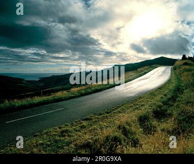 Summit Road und Blick über Okains Bay unter grauen Wolken, Banks Peninsula, South Island, Neuseeland Stockfoto