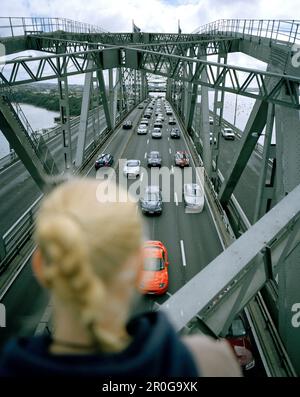 Junge Frau auf Stahlbögen der Harbour Bridge, die auf die Autos auf dem Highway 1 schaut, Auckland, North Island, Neuseeland Stockfoto