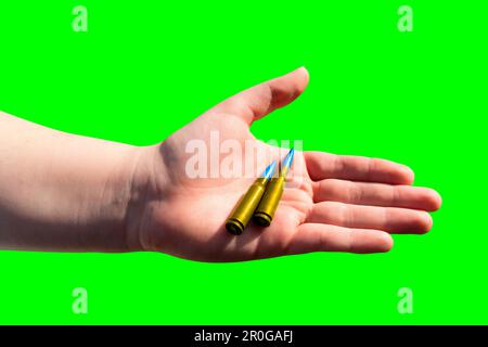 Zwei gelb-blaue Patronen in einer Hand auf grünem Hintergrund (Chroma-Taste). Nationale Symbole der Ukraine. Das Konzept der militärischen Unterstützung für die Ukraine Stockfoto