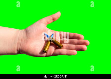 Zwei gelb-blaue Patronen in einer Hand auf grünem Hintergrund (Chroma-Taste). Nationale Symbole der Ukraine. Das Konzept der militärischen Unterstützung für die Ukraine Stockfoto