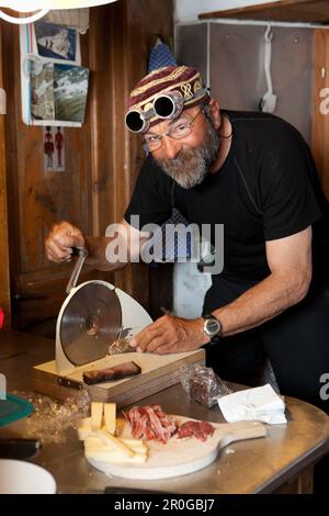 Ein Mann bereitet einen Snack in der Berghütte Cabane de l'A Neuve, Val Ferret, Kanton Valais, Schweiz zu Stockfoto