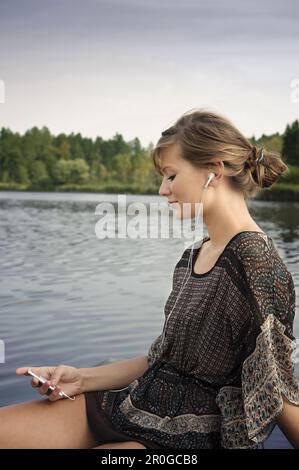 Junge Frau, die Musik am See Starnberg in Bayern hört Stockfoto