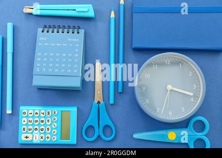 Kalender aus Papier mit Wecker und Schreibwaren auf blauem Hintergrund Stockfoto