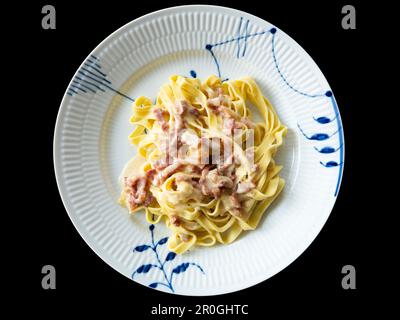 Cremige Nudelpasta Carbonara mit Speck. Draufsicht der Platte isoliert auf schwarzem Hintergrund. Stockfoto