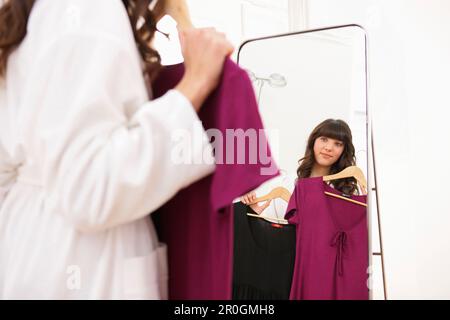 Junge Frau, die Kleider vor dem Spiegel hält, München, Bayern, Deutschland Stockfoto