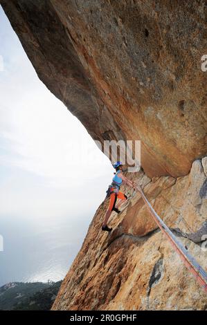 Frau, die unter einem Steinschutzgebiet klettert, Monte San Bartolomeo, Chiessi, Elba Island, Toskana, Italien Stockfoto