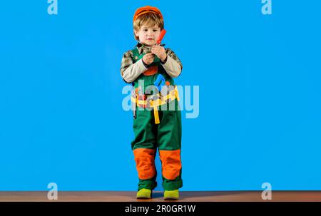 Baumeister mit Schutzhelm und Werkzeuggürtel mit Schraubenzieher. Kind in Uniform und Schutzhelm mit Werkzeuggürtel. Kleiner Mechaniker mit Schraubenzieher. Werkzeuge für Stockfoto