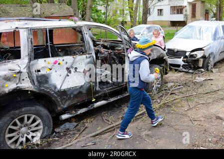 Kinder spielen neben den zerstörten Autos, nachdem die Überreste einer abgeschossen russischen Drohne in der Nähe eines Wohngebäudes in Kiew explodierten. Die Szene nach der Explosion der Trümmer einer gestürzten russischen Drohne in der Nähe eines Wohngebäudes in Kiew am 8. Mai 2023 vor dem Hintergrund der russischen Invasion in der Ukraine. - Das ukrainische Luftkommando sagte, dass alle 35 russischen Drohnen, die auf die Stadt abgeschossen wurden, entdeckt und abgeschossen wurden, während die örtliche Militärverwaltung sagte, dass mindestens fünf Menschen verletzt wurden und Trümmer in mehreren Gebieten Schäden verursachten. Stockfoto