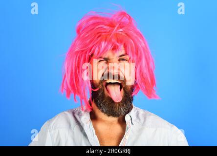 Ein komischer bärtiger Mann mit rosa Perücken zeigt Zunge. Blinzelnder Mann mit Bart und Schnurrbart in Perücke. Gesichtsausdruck. Gefühle und Emotionen. Hipster bei Periwig Stockfoto
