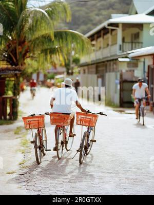 Mann mit Leihfahrrädern auf der Hauptstraße in La Passe, La Digue, La Digue und Inner Islands, Republik Seychellen, Indischer Ozean Stockfoto