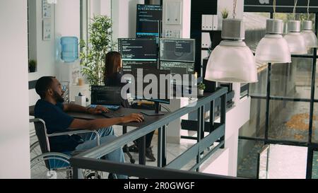 afroamerikanischer Entwickler mit Behinderung, der Computer zum Schreiben von Code benutzt, analysiert Algorithmus in der Software-Agentur. Codierarbeiten an der Benutzeroberfläche mit Datenbank in einem behindertenfreundlichen Büro. Stockfoto