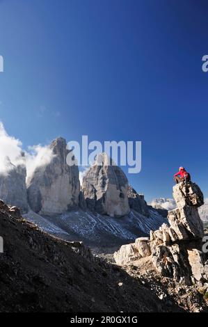 Frau sitzt auf einem Steinturm vor den drei Gipfeln, Tre Cime di Lavaredo, Sexten Dolomiten, Dolomiten, UNESCO-Weltkulturerbe, Südtirol, Stockfoto