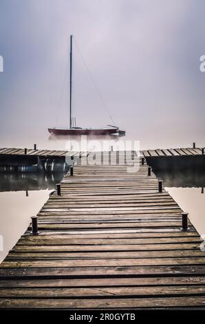 Nebeliger Morgen auf dem See. Boot und Holzpier am Parpocany-See in Tychy, Polen. Stockfoto