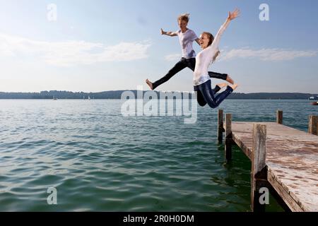 Ein junges Paar springt vom Pier in den Starnberger See in Bayern Stockfoto