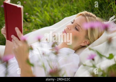 Junge Frau, die auf einer Wiese liegt und liest Stockfoto