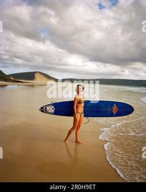 AUSTRALIEN, Queensland, Noosa Heads, Porträt einer Surferin, die lächelt, bevor sie ins Wasser kommt, 40 Mile Beach Stockfoto