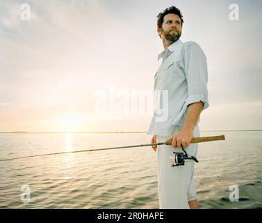 USA, Florida, Fischer holding Angelrute Boot in der Morgendämmerung, New Smyrna Beach Stockfoto