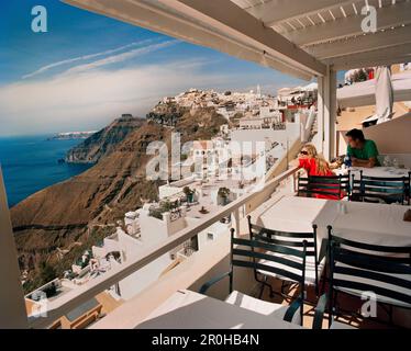GRIECHENLAND, Santorin, Fira, ein touristisches Paar genießt einen Drink und die Aussicht hoch über dem Mittelmeer auf der Insel Santorin Stockfoto