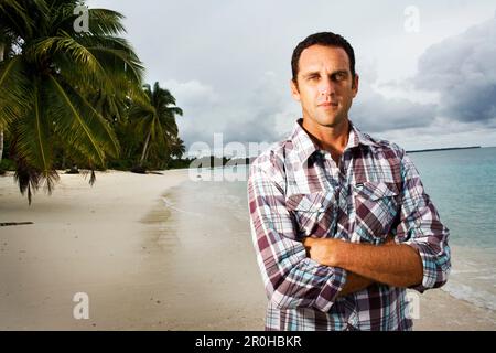 INDONESIEN, Mentawai-Inseln, Kandui Resort, Porträt eines erwachsenen Mannes, der mit gekreuzten Armen am Strand steht Stockfoto