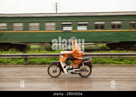 VIETNAM, Hanoi, auf dem Land, ein Mann geht ein Zug auf seinem Moped im Regen Stockfoto