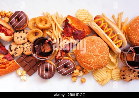 Auf einem weißen Marmorhintergrund verstreute Junk-Food-Tischszene. Auswahl an Speisen zum Mitnehmen und Fast Food. Pizza, Hamburger, pommes Frites, Pommes, Hot Dog Stockfoto