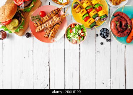 Sommer-BBQ oder Picknick-Essen an der oberen Grenze. Auswahl an Burgern, gegrilltem Fleisch, Gemüse, Obst, Salat und Kartoffeln. Blick von oben auf eine weiße Holzrückseite Stockfoto