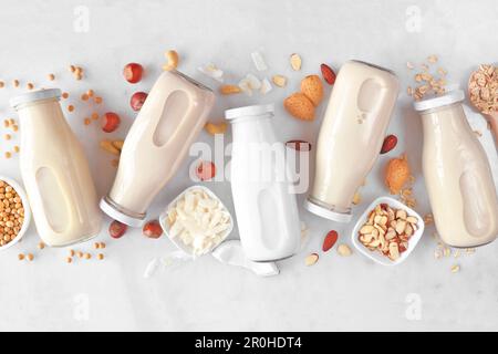 Vegane, pflanzliche Milch ohne Milchprodukte. Vielfalt in Milchflaschen mit verstreuten Zutaten. Blick über einen weißen Marmorhintergrund. Stockfoto