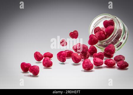 Rote Süßigkeiten in Herzform springen aus einem Glas als Symbol für Liebe und Valentinstag Stockfoto