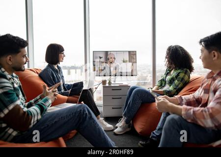 Nahaufnahme verschiedener Fachleute im Bereich der Zusammenarbeit, die an Online-Briefing mit Kollegen mit Hijab und Headset teilnehmen. Glückliche Unternehmer, die die über das Internet erhaltenen Informationen analysieren. Stockfoto