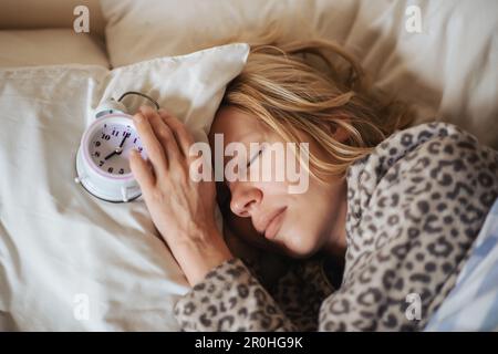 Wecker und schlafende Frau. Der Begriff Schlafprobleme, Schlaflosigkeit, zirkadianer Rhythmus. Stockfoto