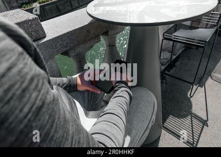 Ein Mann mit einem Smartphone in der Hand sitzt mitten in der Stadt bei Tageslicht Stockfoto