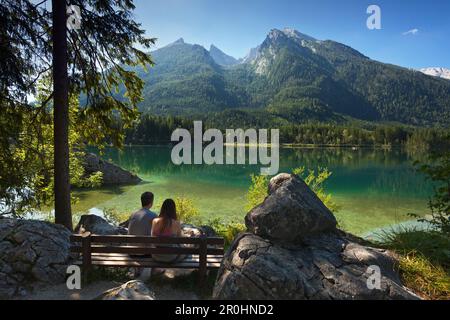 Ein junges Paar sitzt auf einer Bank am Hintersee, Blick auf Hochkalter, nahe Ramsau, Berchtesgaden, Berchtesgaden Nationalpark, Oberbayern, Germa Stockfoto