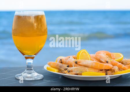 Kaltes Bier im Glas und Garnelen mit Zitrone am Strand Stockfoto